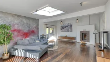 Gemütliches Wohnzimmer mit Kamin, Holzboden, Oberlicht und moderner Wandgestaltung.