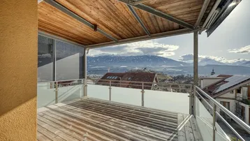Überdachter Balkon mit Holzboden, Glasgeländer und atemberaubendem Bergblick über das Tal.