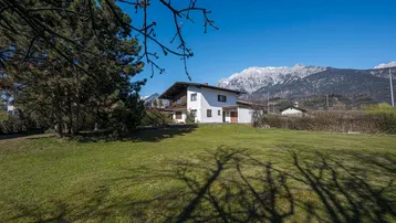 Freistehendes Haus mit großem Garten und beeindruckendem Bergblick unter blauem Himmel.
