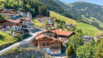 Luftaufnahme eines charmanten Bergdorfes in alpiner Landschaft, mit einem markierten Gebäude im Zentrum.