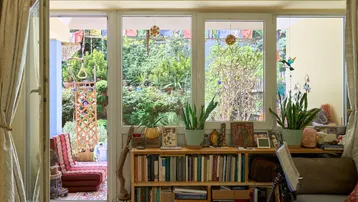 Helles Schlafzimmer mit Bücherregal, Pflanzen und direktem Zugang zu einem grünen Gartenbereich.