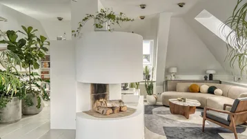 Geräumiges Wohnzimmer im Dachgeschoss mit modernem Kamin, Fliesenboden und vielen Grünpflanzen.