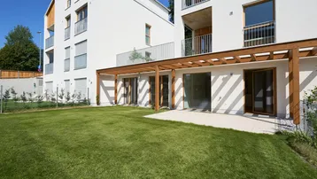 Moderne Wohnanlage mit weißer Fassade, großem Garten und überdachter Terrasse im Erdgeschoss.