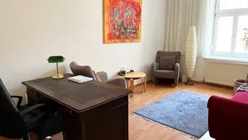 Helles Büro mit großem Schreibtisch, bequemen Sesseln und farbenfrohem Kunstwerk an der Wand.