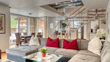Geräumiger Wohn-Essbereich mit bequemer Couch, Esstisch, Holzboden und offener Treppe.