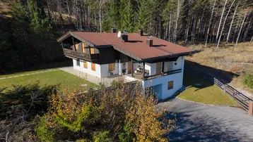 Traditionelles Einfamilienhaus im alpinen Stil, umgeben von Wald und mit Bergblick.