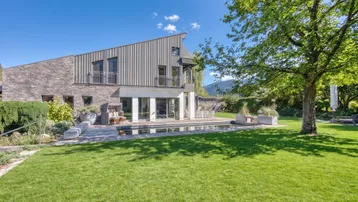 Moderne Villa mit weitläufigem Rasen, Swimmingpool und beeindruckendem Bergblick unter blauem Himmel.