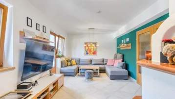 Gemütliches Wohnzimmer mit großem Ecksofa, Fliesenboden und einem traditionellen Kachelofen.