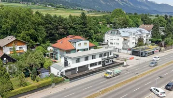 Luftaufnahme eines modernen Gebäudes an einer Straße mit Bergpanorama im Hintergrund.
