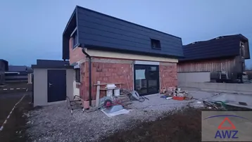 Neubauhaus im Rohbauzustand mit Dach und Fenstern, umgeben von Baustellenmaterialien.