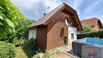 Seitenansicht des Hauses mit Holzfassade und einem Aufstellpool im grünen Gartenbereich.