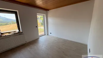 Helles Zimmer mit Holzbalkendecke, Laminatboden und Zugang zum Außenbereich mit Bergblick.
