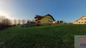 Gelbes Haus auf einem grünen Hügel mit weitem Blick in die Landschaft bei Sonnenuntergang.