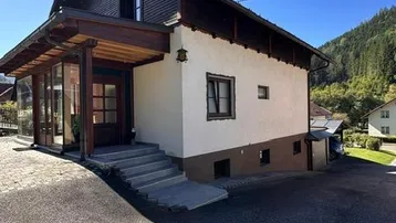 Ansicht des Hauses von vorne mit Eingangsbereich, Auffahrt und Bergblick im Hintergrund.