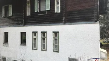 Fassade eines traditionellen Holzhauses mit weiß verputztem Sockel und grünen Fensterläden.