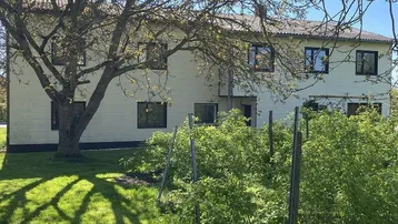 Großes Wohnhaus mit gepflegtem Garten und altem Baumbestand unter blauem Himmel.