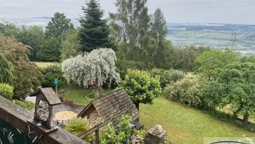 Panoramablick vom Balkon über den gepflegten Garten mit Sitzbereich und weitem Ausblick in die Landschaft.