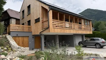 Modernes Holzhaus mit Balkon, Garage und Bergblick in ländlicher Umgebung.