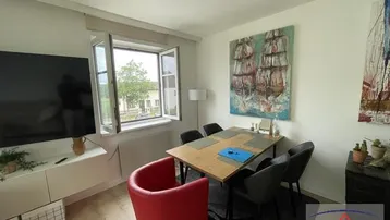 Heller Wohn- und Essbereich mit Esstisch, Fernseher und Blick ins Grüne durch das Fenster.