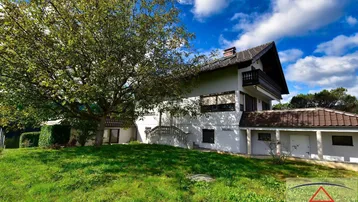 Freistehendes Haus mit Satteldach, umgeben von einem großen grünen Garten und altem Baumbestand.