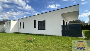 Moderne, weiß verputzte Hausfassade mit Flachdach und gepflegtem Rasen unter blauem Himmel.