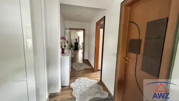 Langer, heller Flur mit Holzboden und weißen Wänden, der zu weiteren Räumen führt.