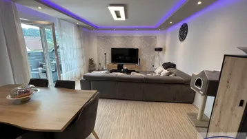 Moderner Wohn-Essbereich mit großem Sofa, Esstisch und Zugang zu einem Außenbereich mit lila Akzentbeleuchtung.