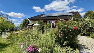 Schönes Einfamilienhaus mit Photovoltaikanlage und blühendem Garten unter blauem Himmel.