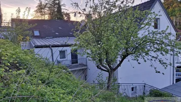 Außenansicht eines gepflegten Hauses mit Balkon und viel Grün in ländlicher Umgebung.