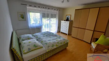 Helles Schlafzimmer mit Doppelbett, großem Kleiderschrank und Blick ins Grüne durch das Fenster.