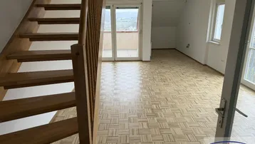 Heller Wohnbereich mit Holztreppe, Parkettboden und Zugang zum Balkon mit Weitblick.