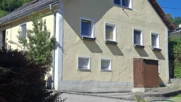 Gelb verputztes Einfamilienhaus mit weißen Fenstern und Satteldach in ländlicher Umgebung.