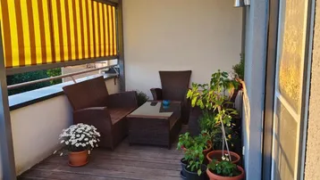 Gemütlicher Balkon mit Holzboden, bequemen Sitzmöbeln und ausziehbarer Markise für sonnige Tage.