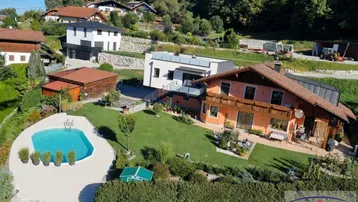 Luftaufnahme eines Hauses mit großem Garten, Swimmingpool und Bergblick in einer grünen Umgebung.