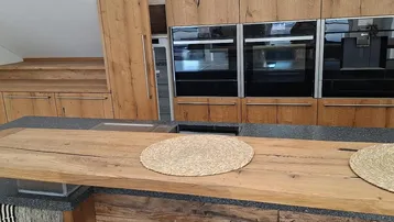 Moderne Küche mit Holzelementen, integrierten Backöfen und einer großen Kücheninsel.
