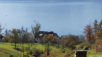 Panoramablick auf einen ruhigen See mit einem Haus und üppiger grüner Landschaft im Vordergrund.