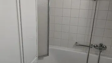 Badezimmer mit Badewanne und Duschvorrichtung, weißen Fliesen und praktischem Stauraum.