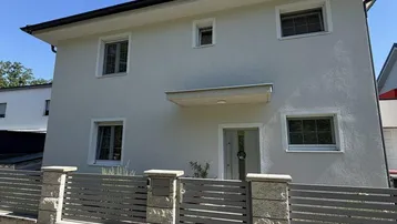 Klare Ansicht der modernen Hausfassade mit Zaun und Eingangsbereich unter blauem Himmel.