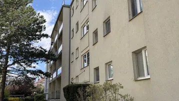 Mehrfamilienhaus mit heller Fassade und gepflegter Grünanlage unter blauem Himmel.
