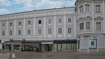 Klassisches Gebäude mit mehreren Etagen und Geschäften im Erdgeschoss, an einer Straßenecke gelegen.