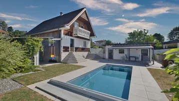 Modernes Haus mit großem Poolbereich und gepflegtem Garten unter blauem Himmel.