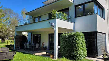 Moderne Hausfassade mit überdachter Terrasse, Balkon und gepflegtem Gartenbereich.