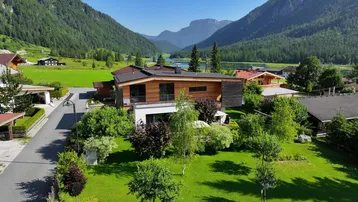 Moderne Villa mit Holzfassade und großem Garten, eingebettet in eine malerische Berglandschaft mit See.