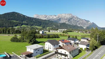 Weitläufige Luftaufnahme einer Wohnsiedlung mit grünen Feldern und majestätischen Bergen im Hintergrund.