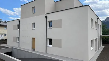 Moderne Neubaufassade mit hellbeigem Putz und Zufahrt zur Tiefgarage im Untergeschoss.
