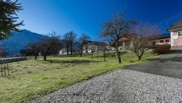 Weitläufige Landschaft mit grünen Wiesen, Obstbäumen und einem beeindruckenden Bergblick im Hintergrund.
