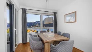 Heller Essbereich mit Holztisch, modernen Stühlen und direktem Zugang zum Balkon mit Seeblick.