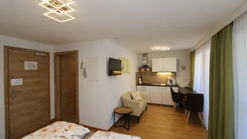 Gemütlicher Wohn-Schlafbereich mit integrierter Küchenzeile, Holzboden und Zugang zu einem Balkon.