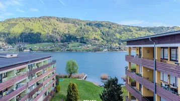 Panoramablick auf den See und die umliegenden Berge mit Wohngebäuden am Ufer.