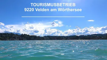 Blick über den Wörthersee mit glitzerndem Wasser und bewaldeter Uferlandschaft im Hintergrund.